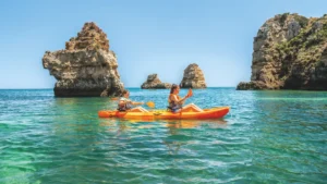 Duas pessoas em kayak exploram as águas cristalinas do Algarve entre impressionantes formações rochosas costeiras, numa experiência tranquila e aventureira com a AlgarExperience.