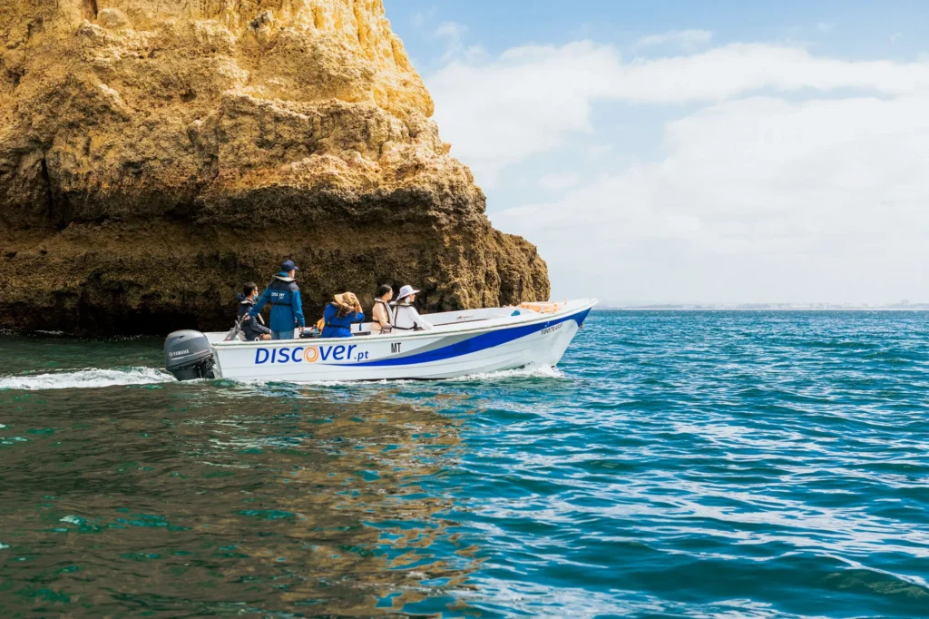 Passeio de barco da Discover Tours junto às falésias douradas da costa de Lagos, com visitantes a explorar o Algarve pelo mar.