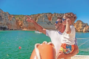 Pai e filho a desfrutar de um passeio de catamarã na Ponta da Piedade, em Lagos, com vista para as águas cristalinas e falésias douradas do Algarve.
