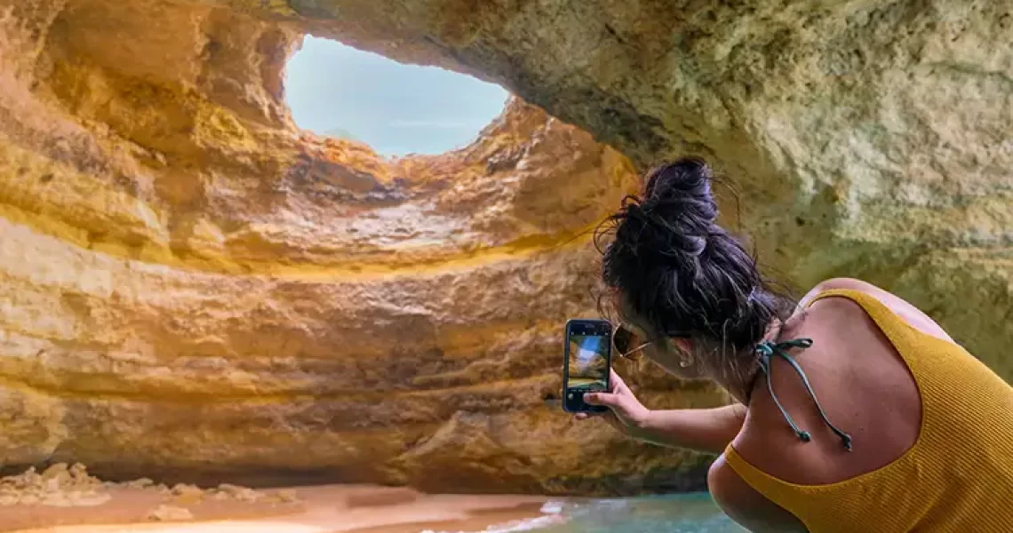 Frau fotografiert eine der Höhlen der Algarve - Algar de Benagil